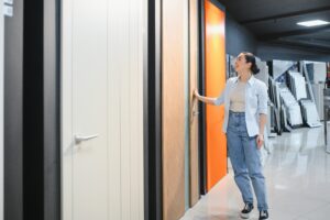 Woman browsing modern door designs at a timber door supplier showroom in Malaysia, showcasing solid timber door choices.