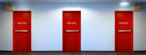 Three red fire exit doors in a hallway, showcasing fire rated door design by a fire rated door supplier in Malaysia.